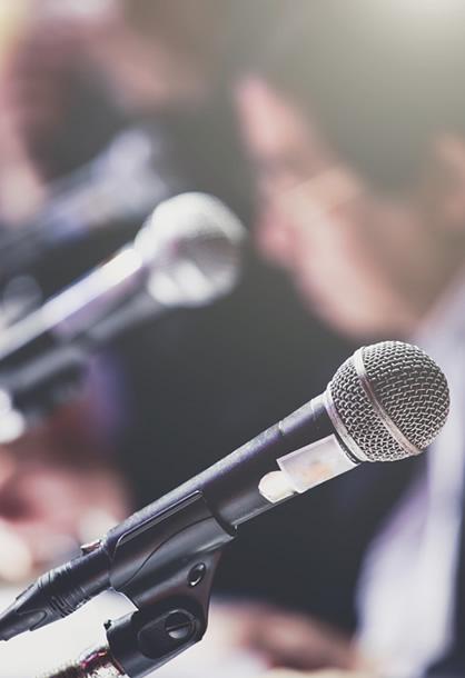 Microfoni pronti per una conferenza stampa con persone sullo sfondo.