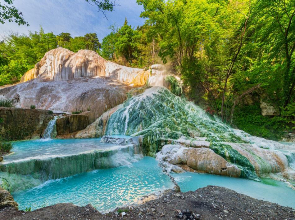 Natural thermal waterfalls in greenery, with blue water and limestone rocks.