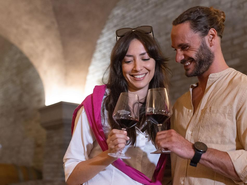 Happy couple toasts with red wine glasses in a cellar.