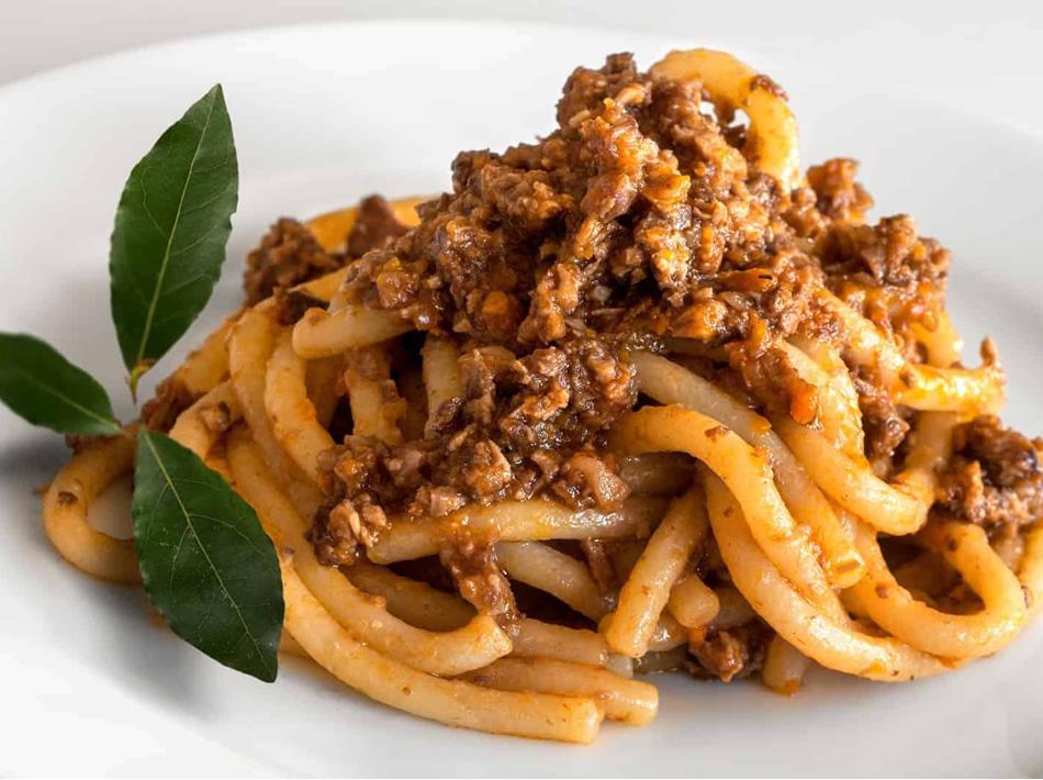 Pasta with meat sauce and bay leaves on a white plate.