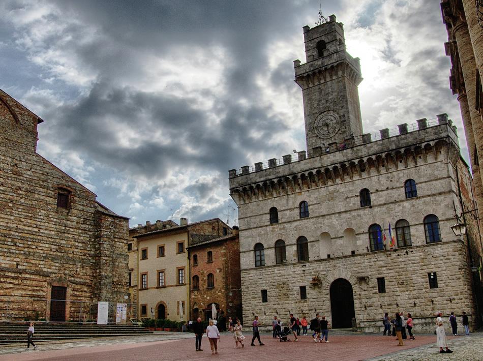 Piazza con edifici storici e torre dell'orologio sotto un cielo nuvoloso.