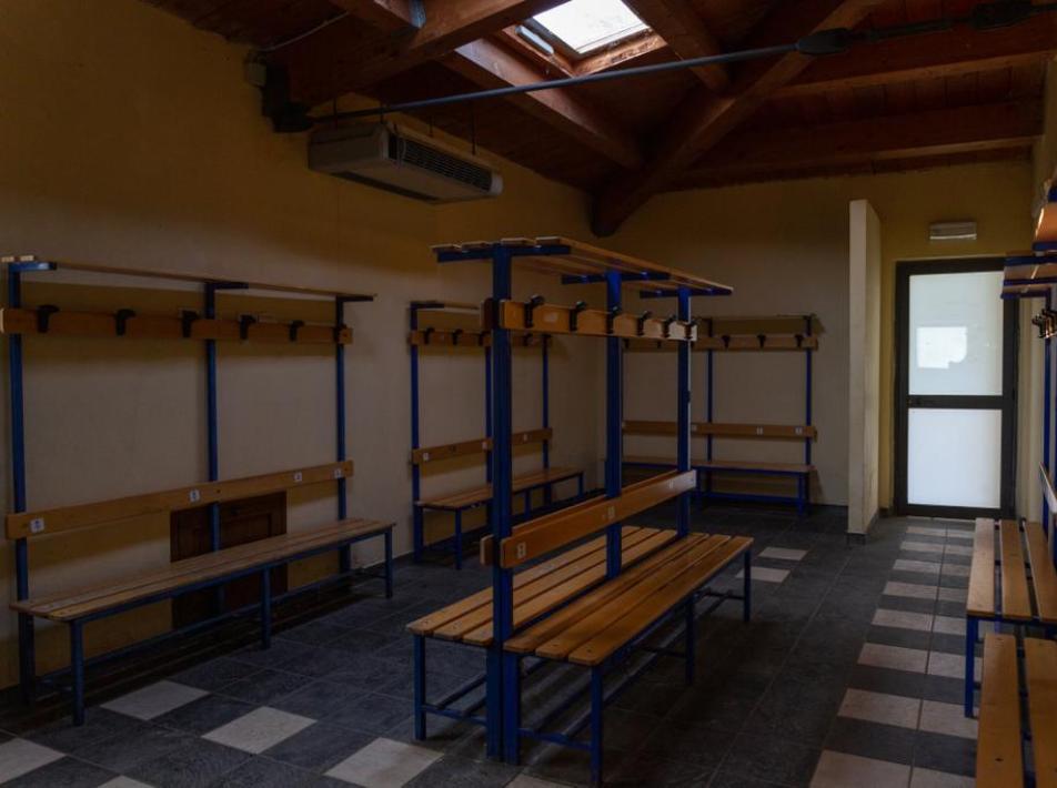 Spogliatoio con panche di legno e ganci per appendere, illuminato da lucernari.