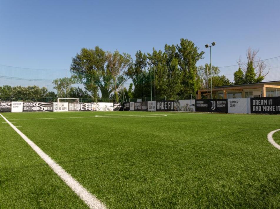 Campo da calcio con erba sintetica, recinzioni pubblicitarie e rete di protezione.