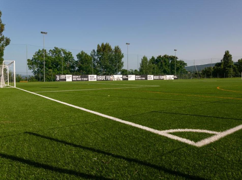 Campo da calcio in erba sintetica con rete e cartelloni pubblicitari.