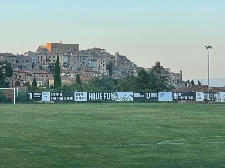 Campo da calcio con sfondo di una città storica, Juventus Academy Summer Camp.