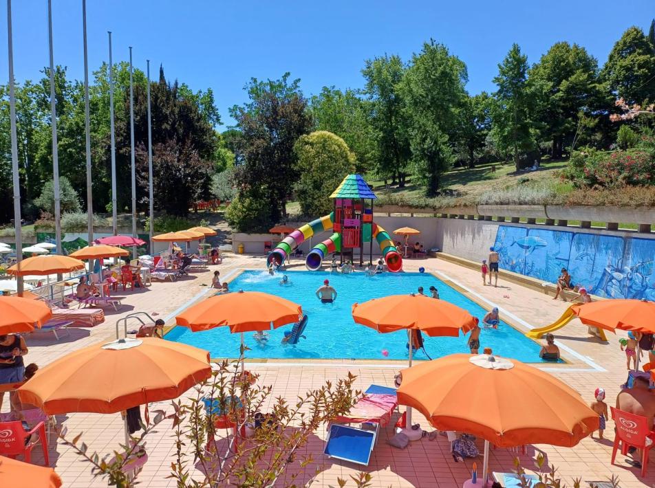 Piscina all'aperto con scivoli, ombrelloni arancioni e persone che si divertono.