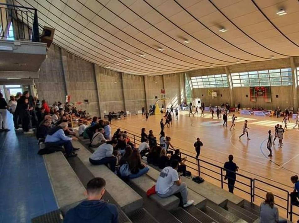 Partita di basket in palestra con spettatori sugli spalti.