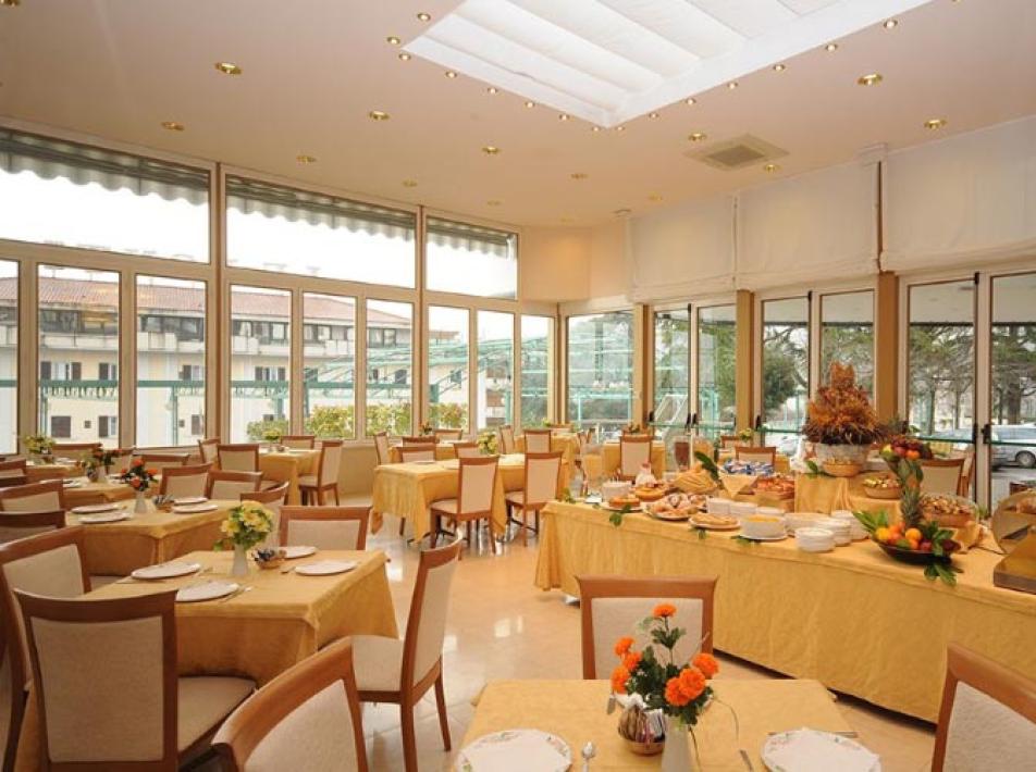 Elegante sala da pranzo con buffet, tavoli apparecchiati e grandi finestre panoramiche.