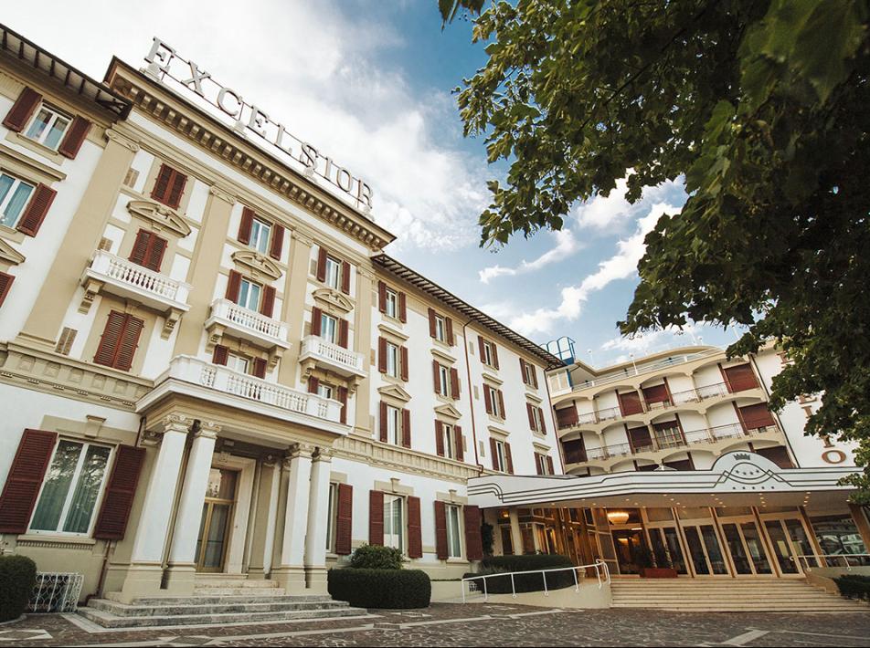 Elegante hotel Excelsior con facciata classica e balconi, circondato da alberi.