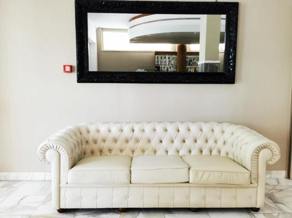Divano bianco elegante sotto uno specchio nero in una stanza luminosa.