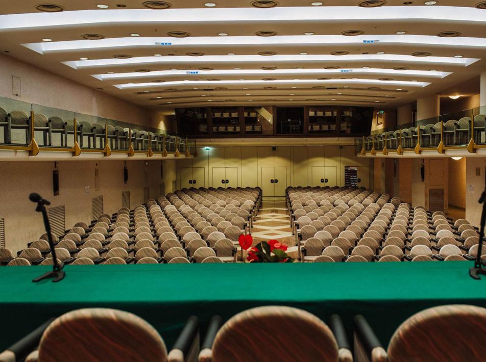 Conference room with chairs in rows and microphones on the green table.