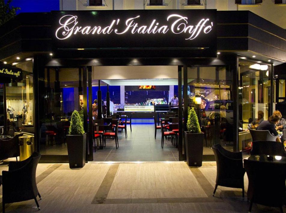 Elegant Italian cafe with red and black chairs, illuminated at night.